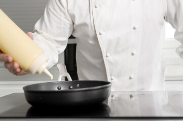 Close up of chef hand pouring sauce from gravy bottle into frying pan at commercial kitchen. High quality photo