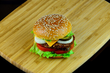 Beef Angus Cheese Burger with fresh Tomatoes, Onion, Jalapeno and Lettuce Leaves on the wooden board in black background