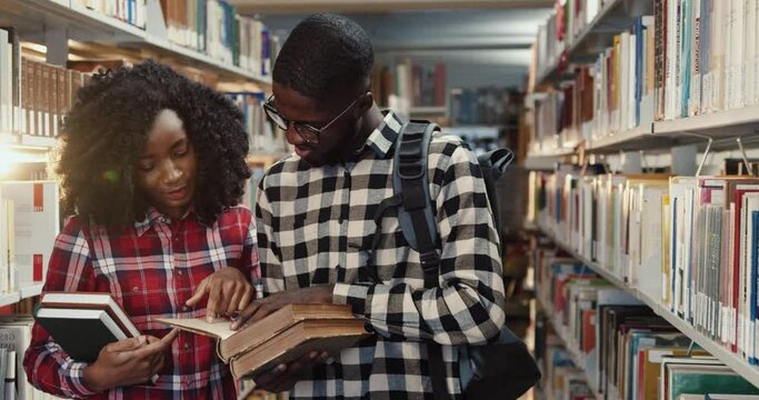 Close up of young African American couple of students standing in library and reviewing interesting book and discussing its contents.