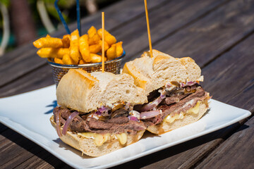 A steak sandwich and fries served on a white plate