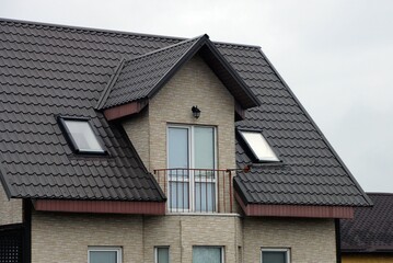 open iron balcony on the gray  brick wall of the house under the brown tiled roof against the sky