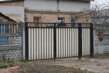 a large white metal gate with black iron bars and part of a gray stone fence outside