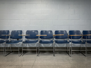 A Line of Blue Empty School Chairs Lined-Up Against a Brick Wall in an Empty Room