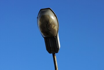 one old dirty gray lantern on an iron pole on the street against a blue sky