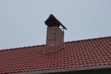  one brown brick chimney on the red tiled roof of a private house against the gray sky
