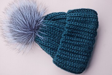 blue green winter woolen hat with a gray fluffy pompom lies on a brown table