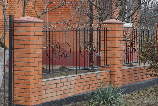 part of the red fence wall of black iron bars and  bricks on the street