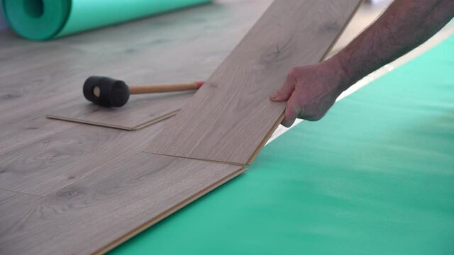 man installing laminate flooring and connecting the laminate planks together.