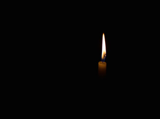 A white candle light burning in the dark to the right of the frame.