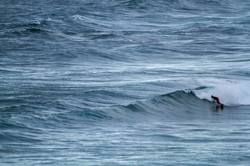 A surfer sportingly rides down a wave on a beach in Portugal on the Atlantic Ocean