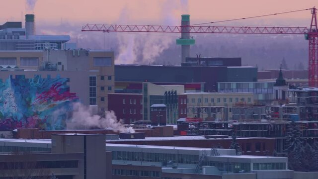 4k Winter twilight University of Alberta buildings rooftops covered with snow steam louds puffing with faded blurred background forest trees and some residential housing and red construction crane