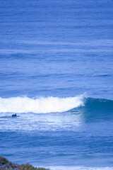 A surfer paddles on his surfboard towards a breaking approaching wave on a beach in Portugal on the Altantic Ocean