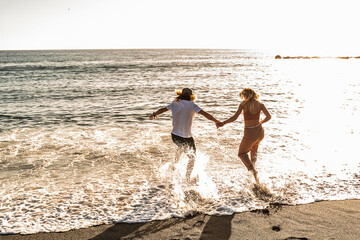 Couple running on a sandy beach together, holding hands, having fun on a sunset beautiful time....