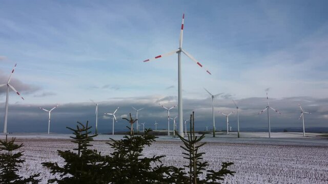 Ascending aerial shot of fir trees and wind turbines farm in background on snowy winter day during Christmas time.