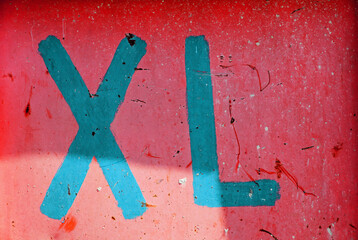 Auf einer roten Metallwand seht groß in türkis-blauer Farbe XL