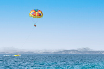 Fototapeta na wymiar Couple of tourists flying on a colorful parachute on blue sky background. Copy space, holiday fun activities. Sea summer recreation - Turkey.