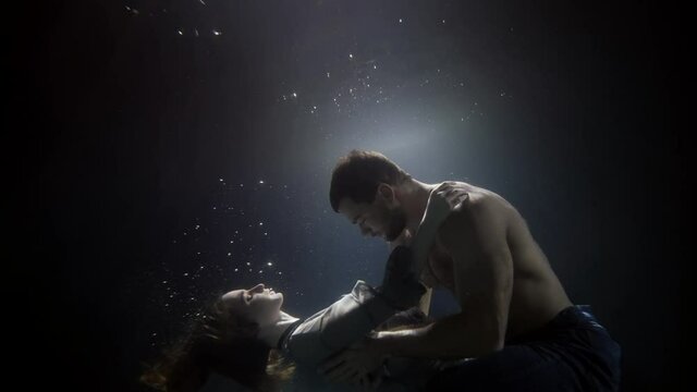A man passionately touches and hugs his girlfriend underwater, lovers deep inside on a dark background. Bubbles float around them. They spin beautifully.