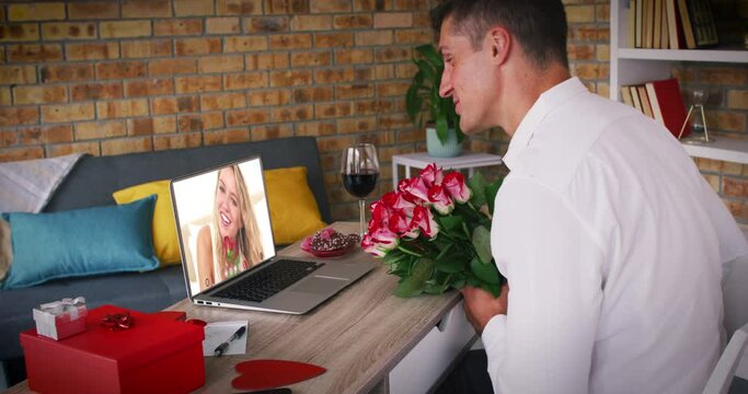 Caucasian couple holding flowers making valentines date video call man blowing kiss to woman on lapt