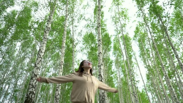 A young woman spins in a birch forest. The girl is glad to be in nature.