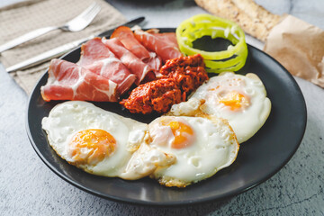 close up view on sunny side up eggs prosciutto coppa Capocollo dry meat and homemade ajvar paprika salad in plate on the table as dinner or breakfast meal