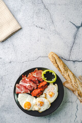 Top angle view on sunny side up eggs prosciutto coppa Capocollo dry meat and homemade ajvar paprika salad on the table as dinner or breakfast meal with copy space