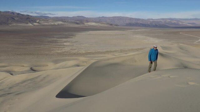 Man walking up on a sand dune with mountain and clouds in the background, Eureka Dunes, Death Valley National Park