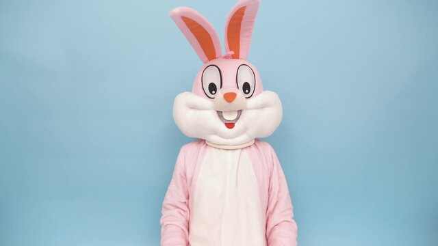 Easter bunny or rabbit or hare with basket of colored eggs, shows thumb finger up, having fun, dancing, celebrates Happy easter. Easter rabbit isolated on blue background