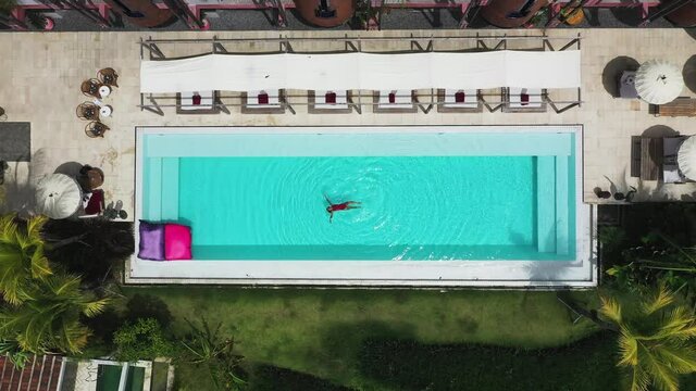 Female Swimming Looking Up At The Sky At Shore Amora Canggu Hotel Pool In Bali, Indonesia, Aerial Rising Reveal Shot