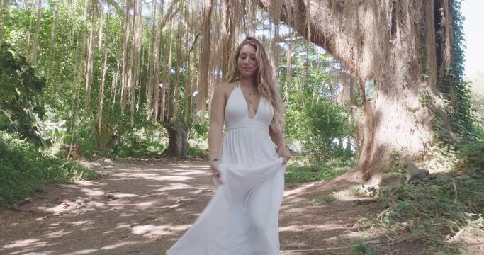 Gorgeous long haired woman walks in tropical forest in white dress
