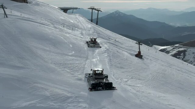 Two snow groomers a top mountain ski resort prepping empty slopes. Aerial high angle.