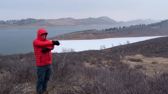 Senior male hiker wearing down jacket and mittens is try to warm up - Lory State Park and Horsetooth Reservoir in northern Colorado at foothills of Rocky Mountains in winter scenery with falling snow
