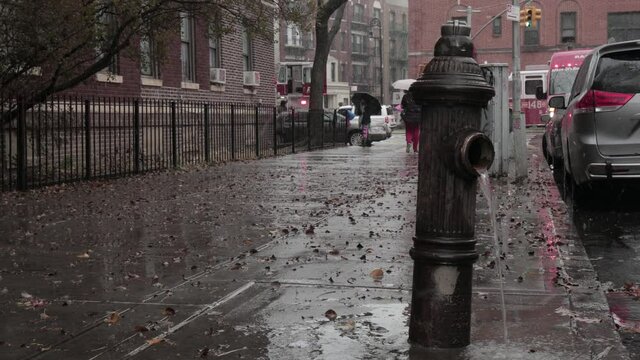Fire hydrant spilling water on a Brooklyn sidewalk on a snowy, rainy, cloudy winter day - Medium close up shot