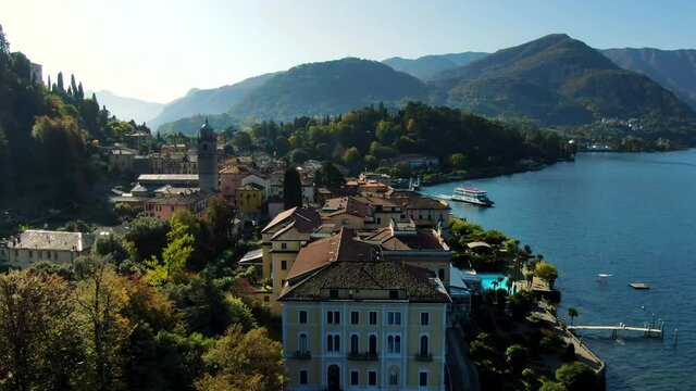 Approaching Bellagio, Lake Como in Italy. Mountains visible in the background and a boat leaving the local pier. Sunny day, some sun flairs visible in the shot.