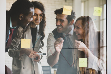 Group of four professional multiracial businessmen and businesswomen brainstorming and discussing by writing graph with a marker on glass wall to explain company financial status to plan strategy