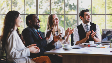 Group of four professional multiracial businessmen and businesswomen sitting and clapping hands to celebrate the new project ideas in a partners company meeting at the modern office working table