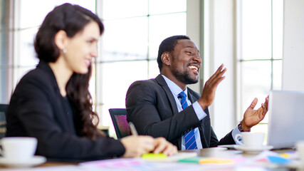 Portrait of a happy handsome African businessman clapping a hand in a multiracial meeting at the conference room with cute smiling with businesswoman foreground. Concept of happiness business work
