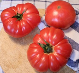 Three red fresh tomatoes on a wooden board and on a towel for cooking