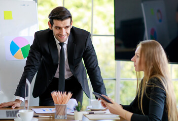 Successful handsome young adult caucasian businessman leader standing in front of the multiracial meeting looking at the caucasian businesswoman and concentrated listening to new problem-solving idea