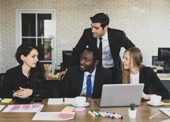 Attractive young adult caucasian businessman leader consulting with concentrated multiracial colleagues that gathered in front of a laptop and looking at caucasian businesswoman that share her idea