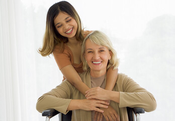 Happy mix skin family living together, adopted asian daughter  cuddle caucasian mother sitting on a wheelchair with smiles. Close up