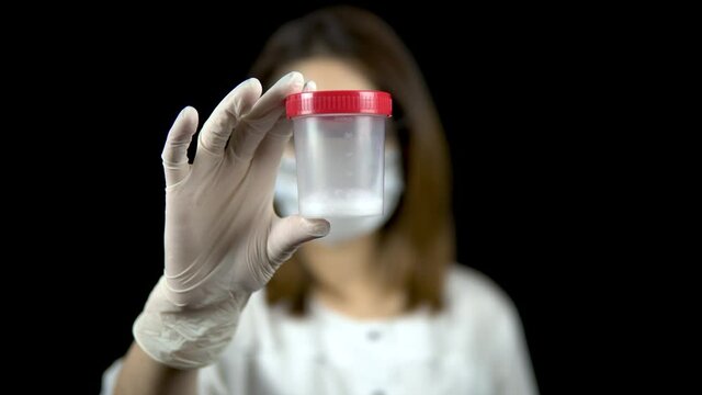 Sperm in a test bank close-up. Woman doctor holds out a jar of sperm to the camera on a black background.