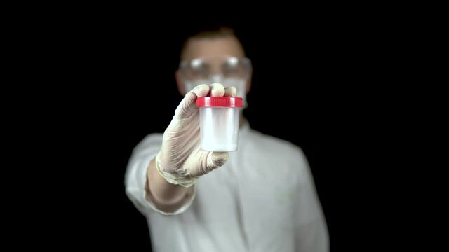 Sperm in a test bank close-up. Woman doctor holds out a jar of sperm to the camera on a black background.