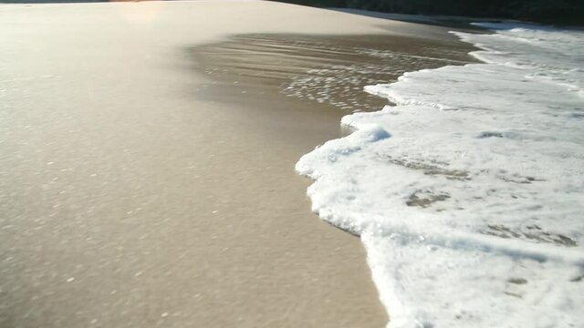 Pan traking of some waves hitting the shore of a beautiful beach with golden sand in the morning of a vacation