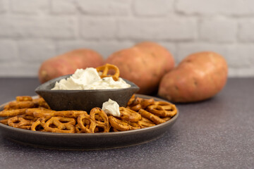 Healthy sweet potato pretzels in a tray with chive and onion cream cheese dip on a dark table and a white background.
