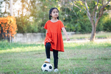 A young Asain girl playing football with her big black dog outside the grass ground in the yard in the evening. ,