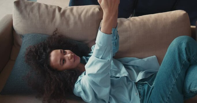 Cinematic move around beautiful young mixed race woman talking to friend using smartphone video call at home on sofa.