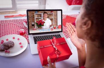 Diverse couple making valentines date video call on laptop holding gift and flowers