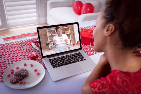 Diverse couple making valentine's date video call the man on laptop screen holding marry me sign