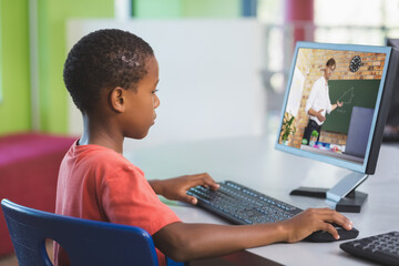 African american schoolboy using computer on video call with male teacher