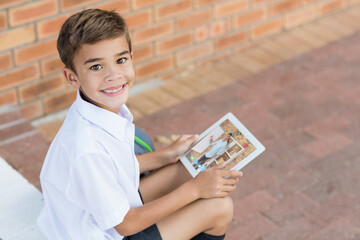 Portrait of smiling caucasian schoolboy using digital tablet on video call with male teacher